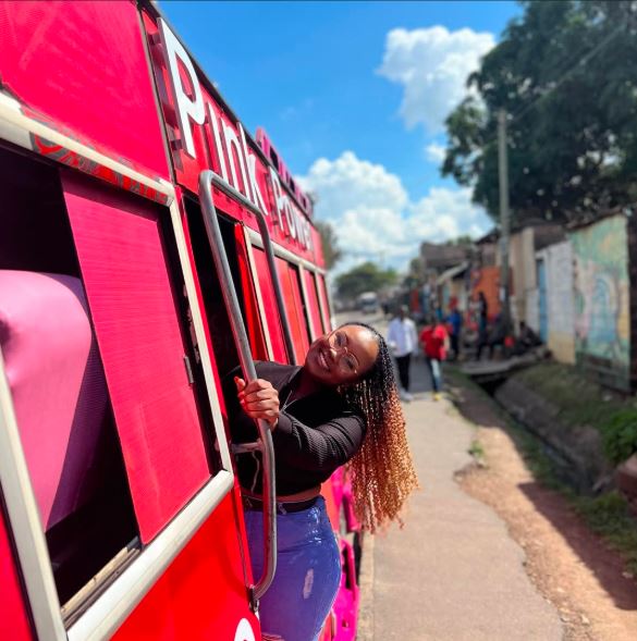 a lady standing on a pink nganya matatu
